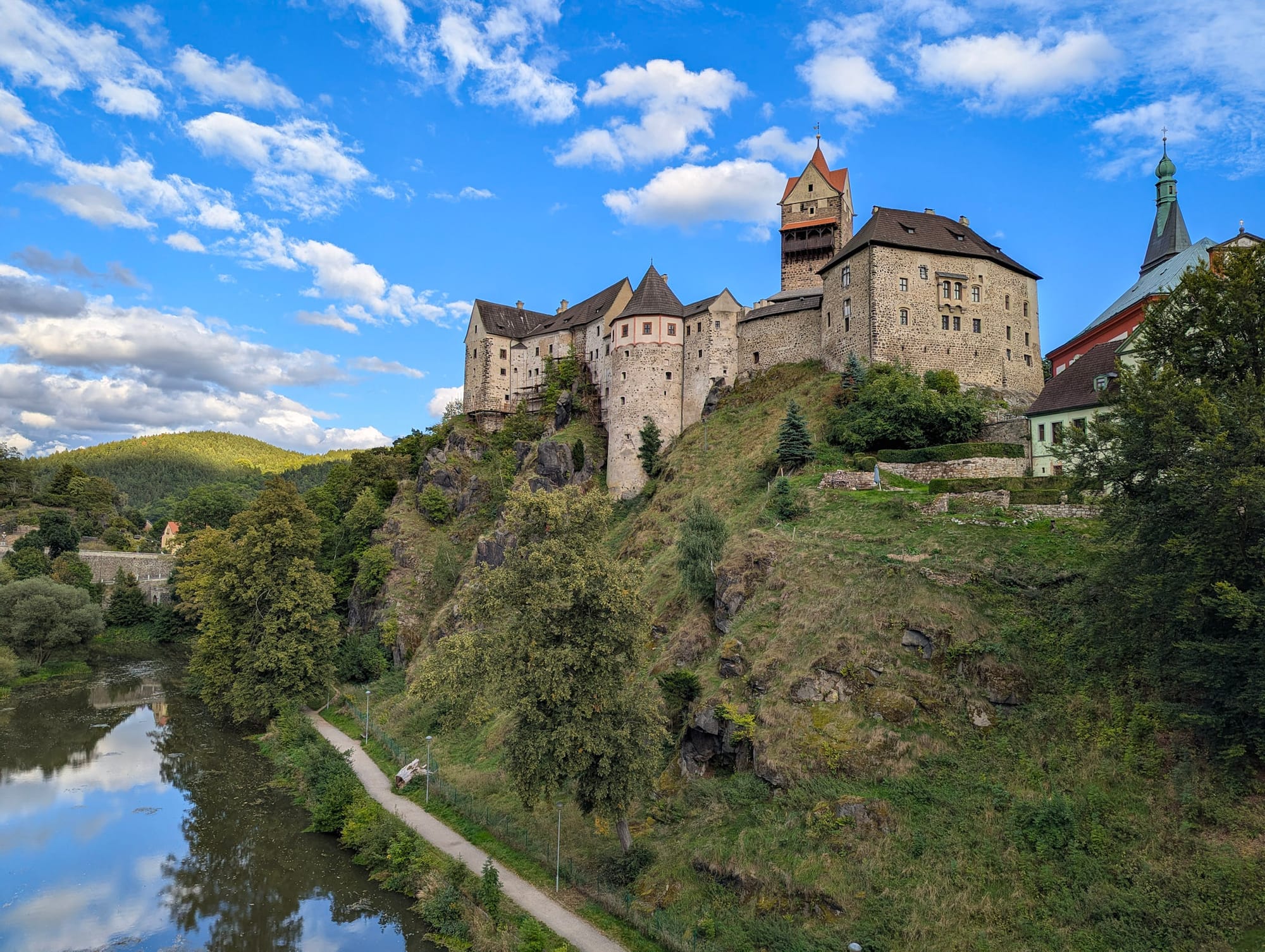 Eine Burganlage auf einem Felsen, darunter fließt ein Fluss entlang. 