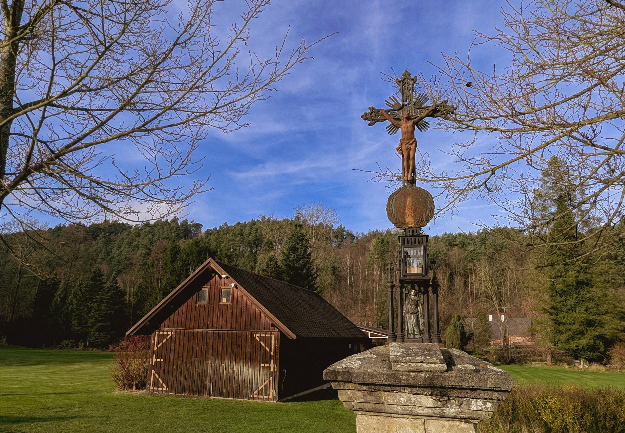 Ein Holzhaus neben einem Steinkreuz in einem böhmischen Dorf.