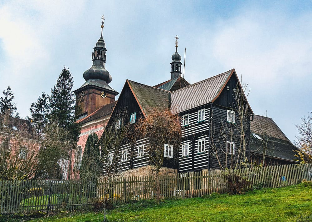 Eine Kirche neben einem holzgetäfelten Wohnhaus in einem tschechischen Dorf.